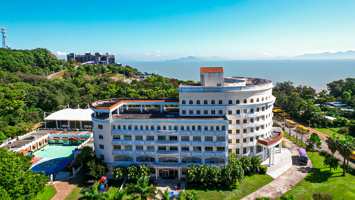 Zhuhai Qiao International School campus showing a white circular building with lush greenery and the sea in the background.