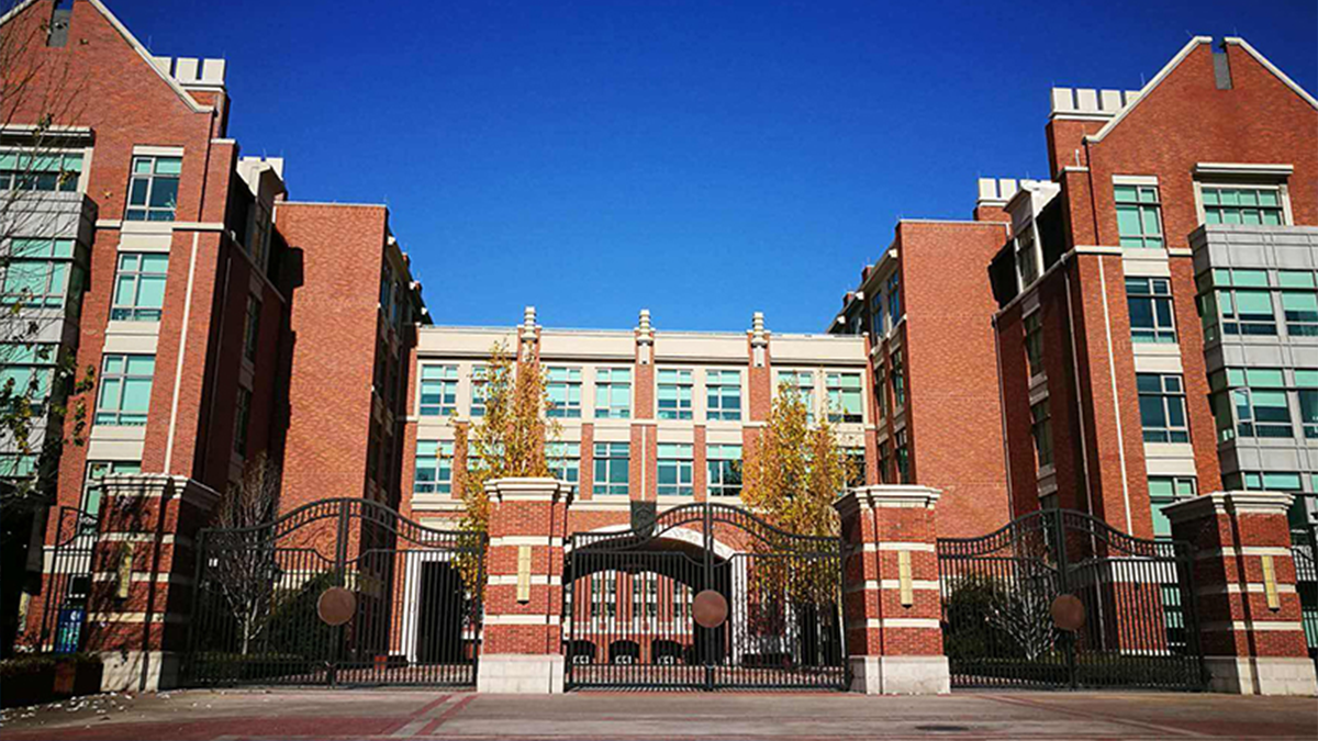 Beijing Keystone Academy campus featuring red brick buildings with ornate entrance gates and a clear sky.
