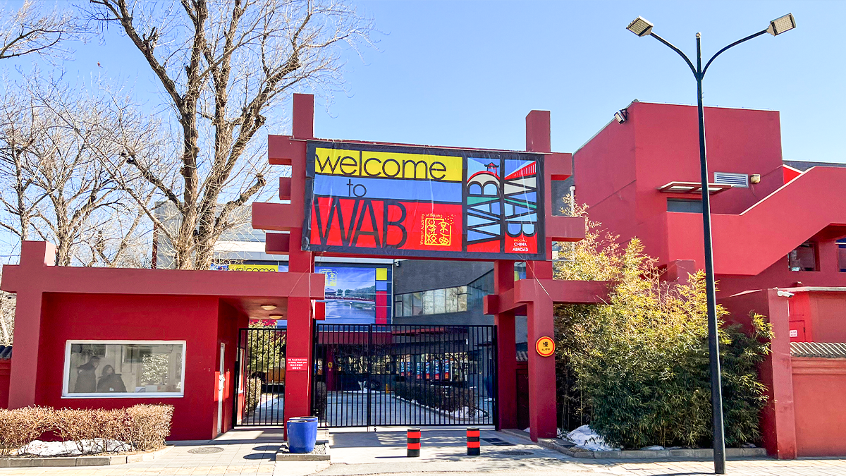 Western Academy of Beijing campus featuring modern red buildings, gated entrance, and prominent multilingual school branding.