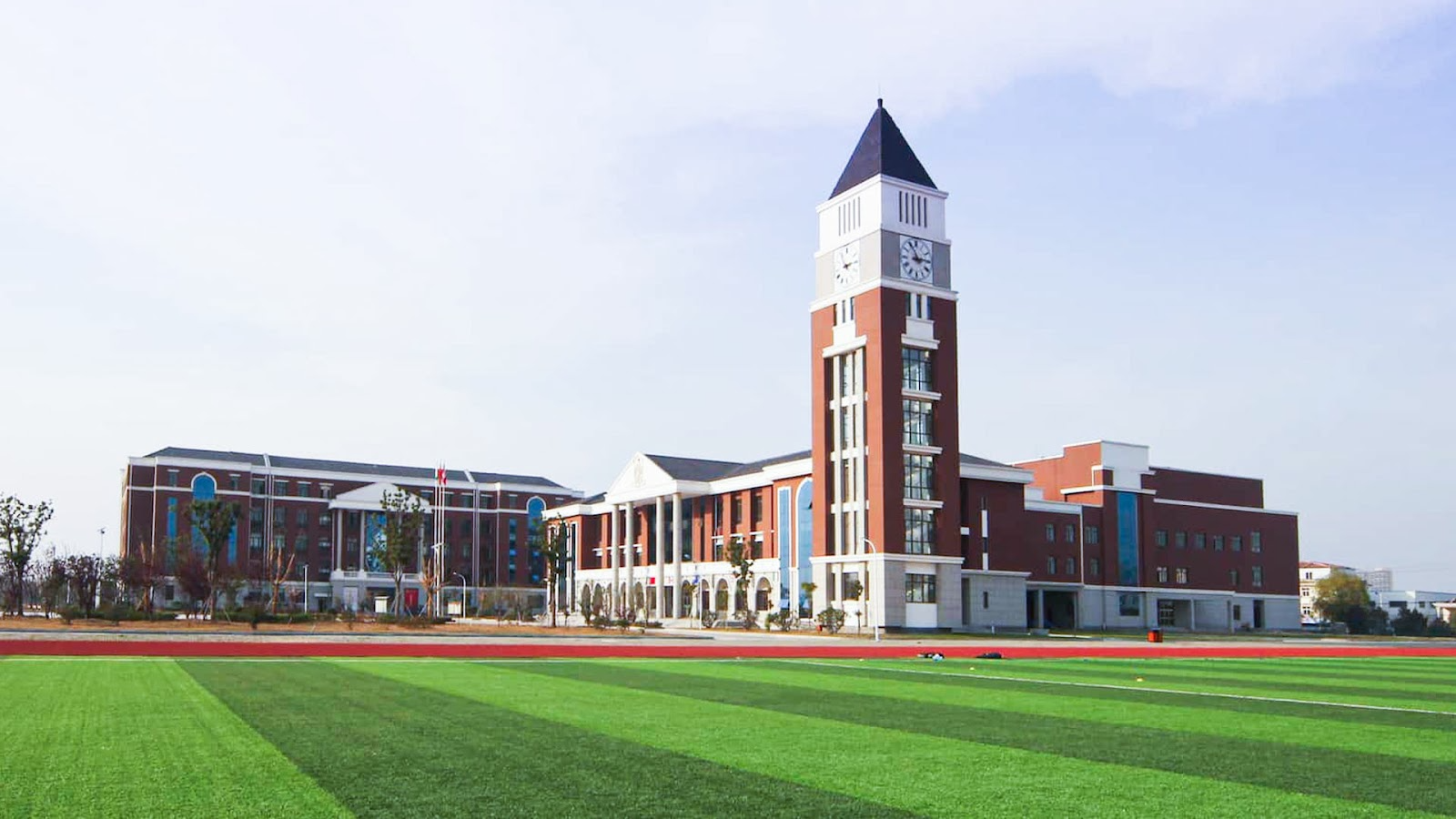 Modern international school campus with distinctive clock tower and green athletic field.