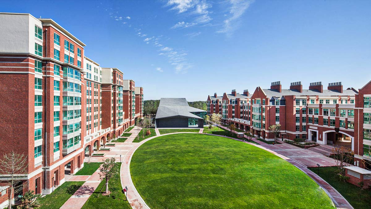 Beijing Keystone Academy campus showcasing red brick buildings surrounding large central green lawn area.