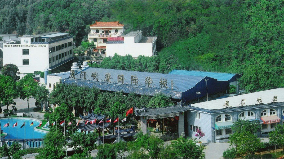 Manila Xiamen International School MXIS hillside campus with swimming pool international flags and lush green forest surroundings.