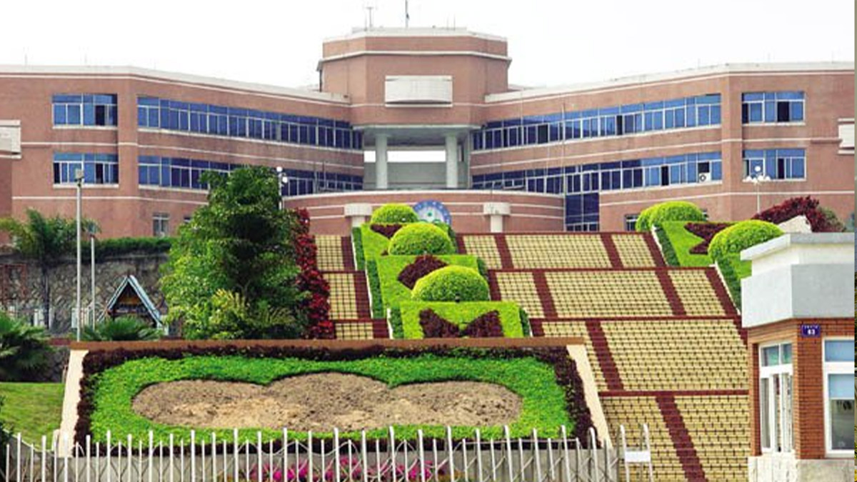 Xiamen Yingcai School red brick campus building with blue glass windows and decorative topiary garden landscape entrance.