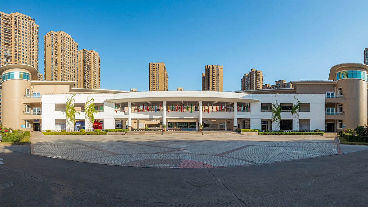 Xiamen International School XIS modern campus courtyard with white curved building colorful flags and spacious plaza entrance.