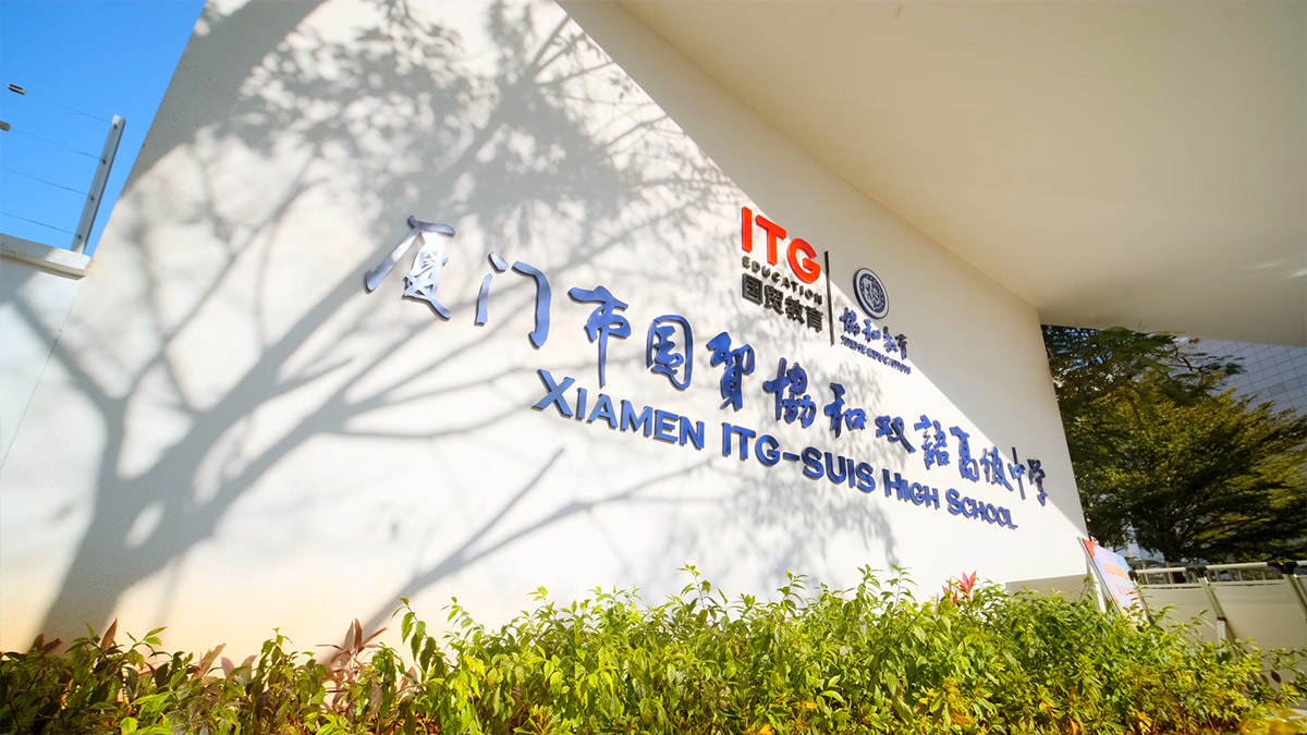 Xiamen ITG-SUIS High School white entrance wall with bilingual signage red ITG logo and landscaped garden with tree shadows.
