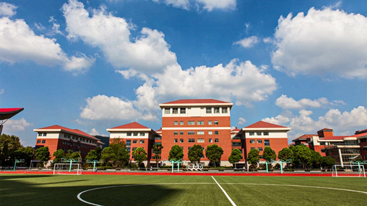 Wuxi No.1 High School orange buildings overlooking green soccer field under blue sky