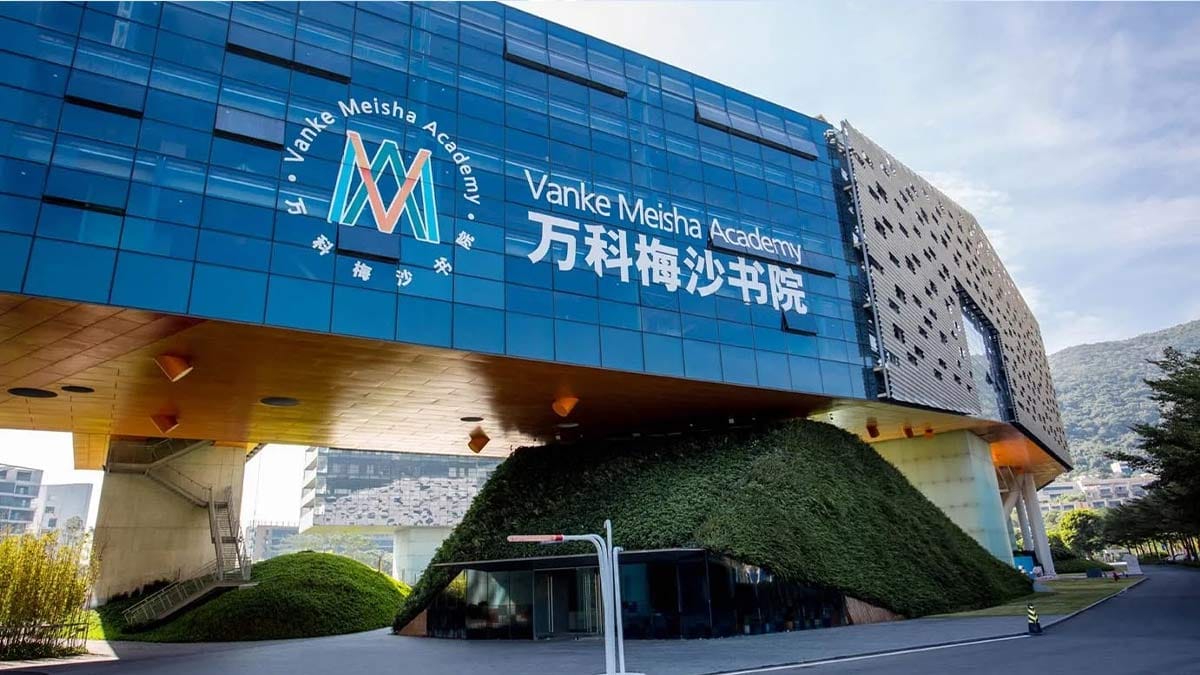 Vanke Meisha Academy futuristic blue glass building with green hillside landscaping