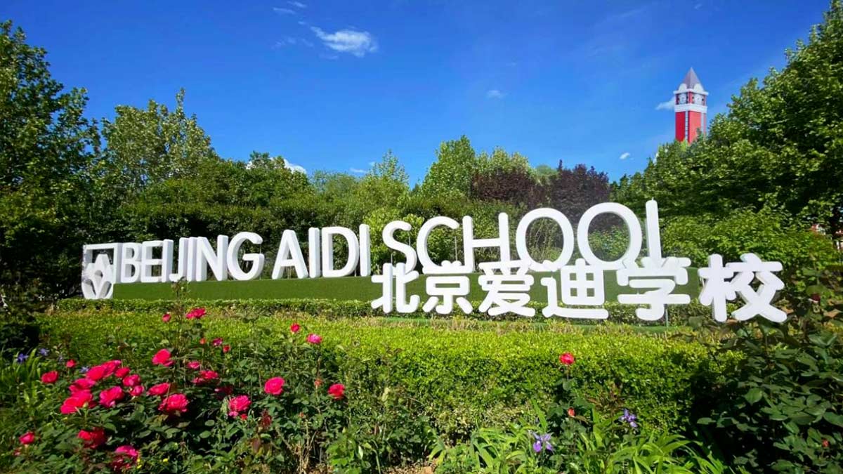 Beijing Aidi School outdoor sign surrounded by roses and greenery with clock tower