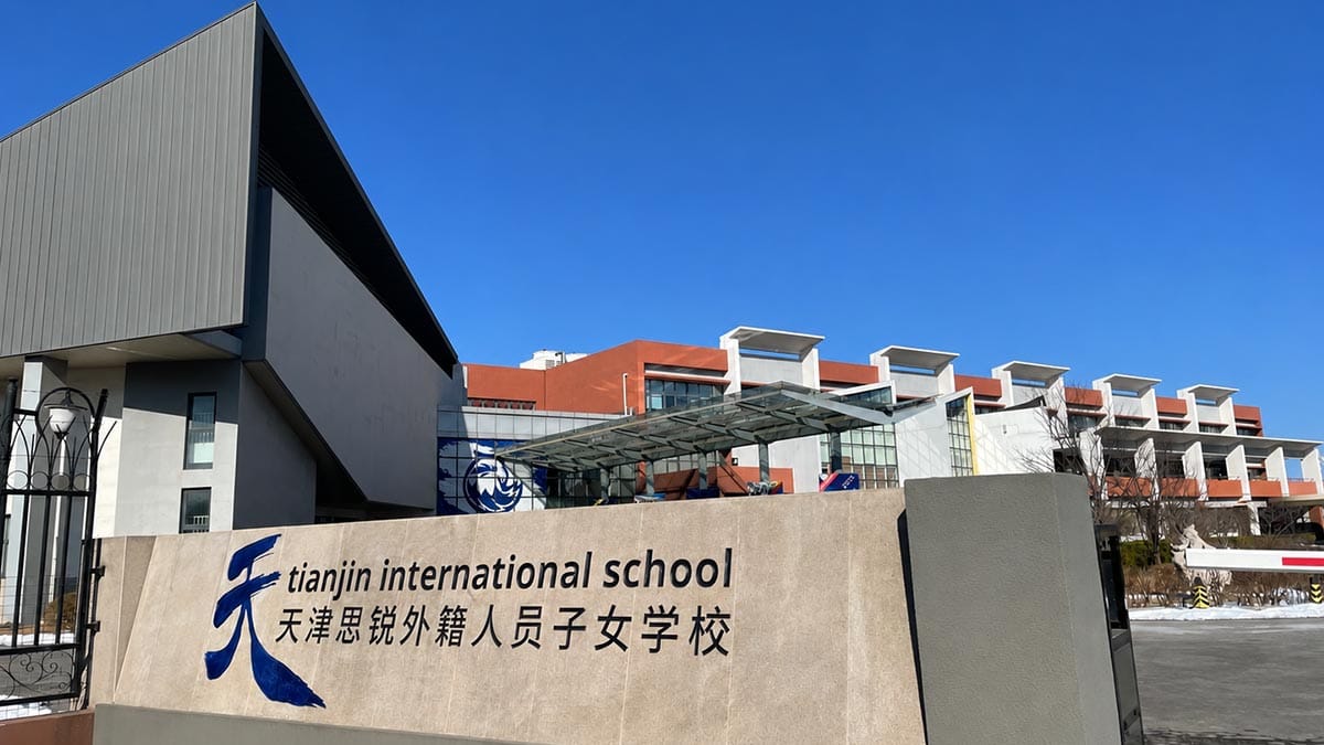 Tianjin International School bilingual name wall with red campus buildings behind