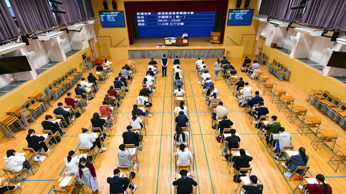 HKDSE examination hall — students sitting the Chinese Language paper at a Hong Kong school, with exam details displayed on the screen at the front