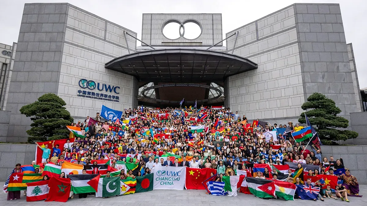 UWC Changshu China (常熟世界联合学院) full school photo — hundreds of international students holding country flags on the steps of the United World College Changshu China campus building in Jiangsu Province