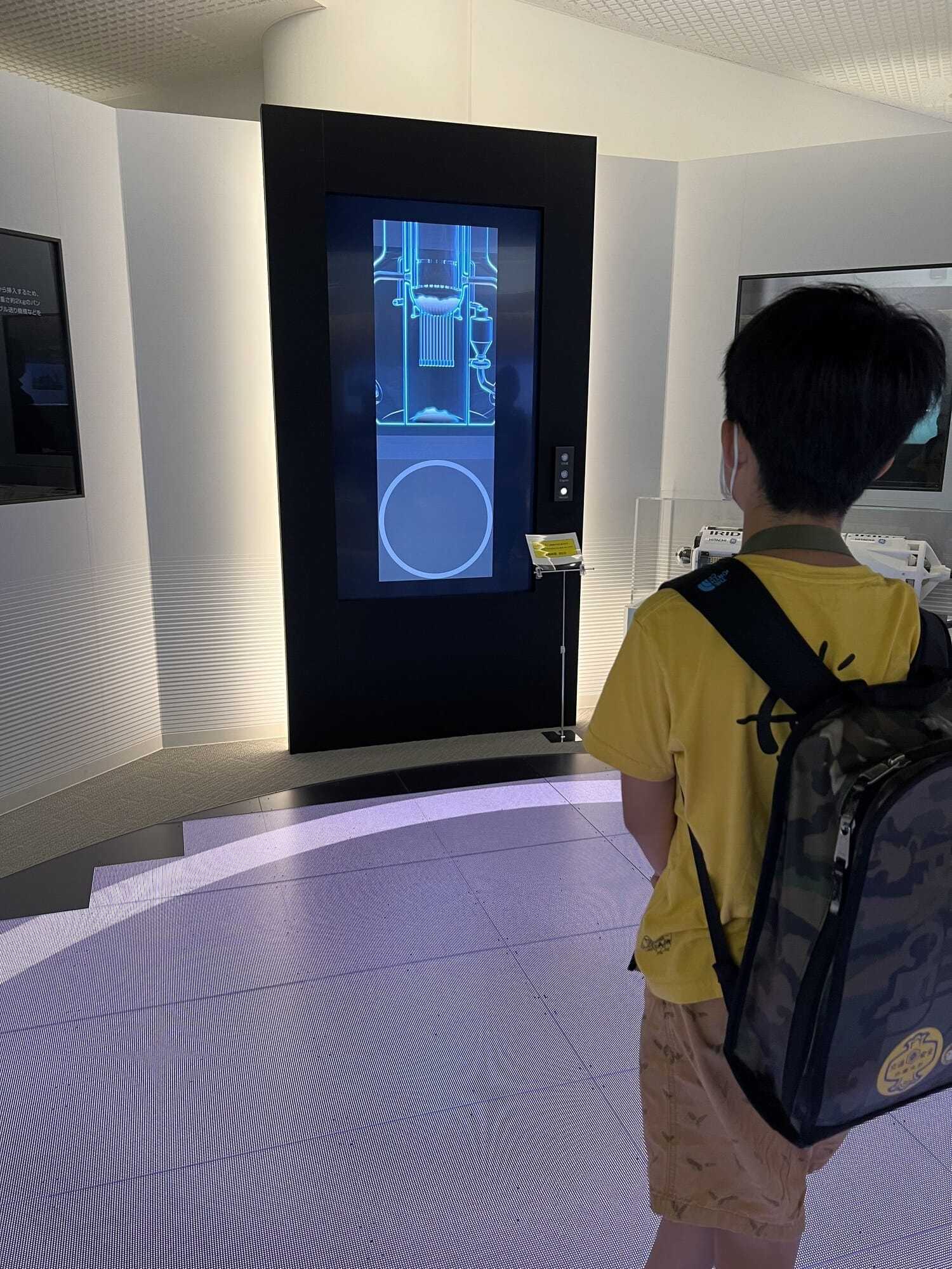 A child watching a multilingual touchscreen exhibit showing a reactor cross-section at the TEPCO Decommissioning Archive Center