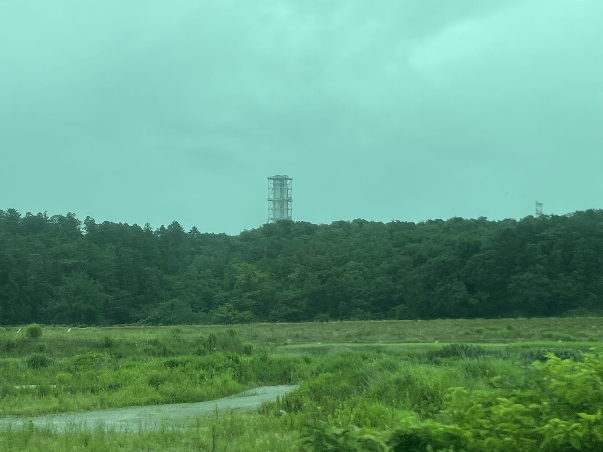 Exhaust stack of the Fukushima Daiichi Nuclear Power Station seen over woodland from a Joban Line train window