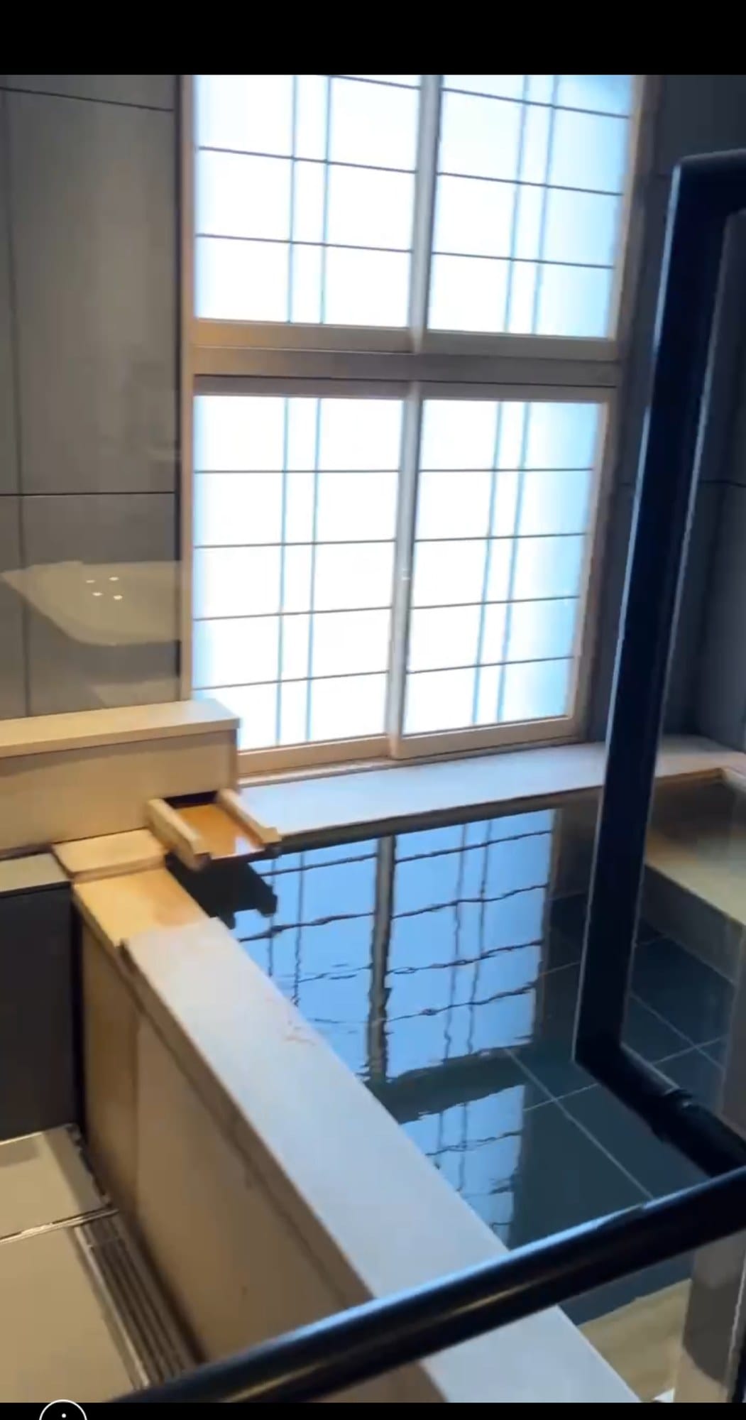 An indoor hinoki-framed private hot-spring bath filled with dark mineral water beside a shoji window at FUFU Kyoto