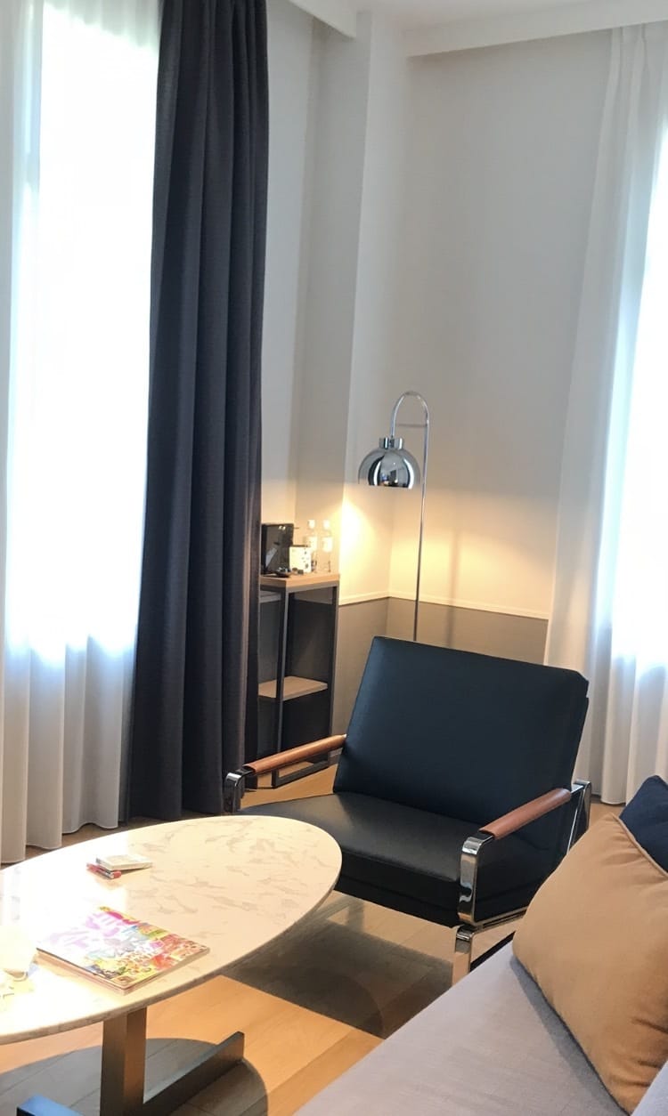 Schoolhouse room at THE GATE HOTEL Kyoto Takasegawa — leather armchair and marble table beside a tall window in the former Rissei Elementary School