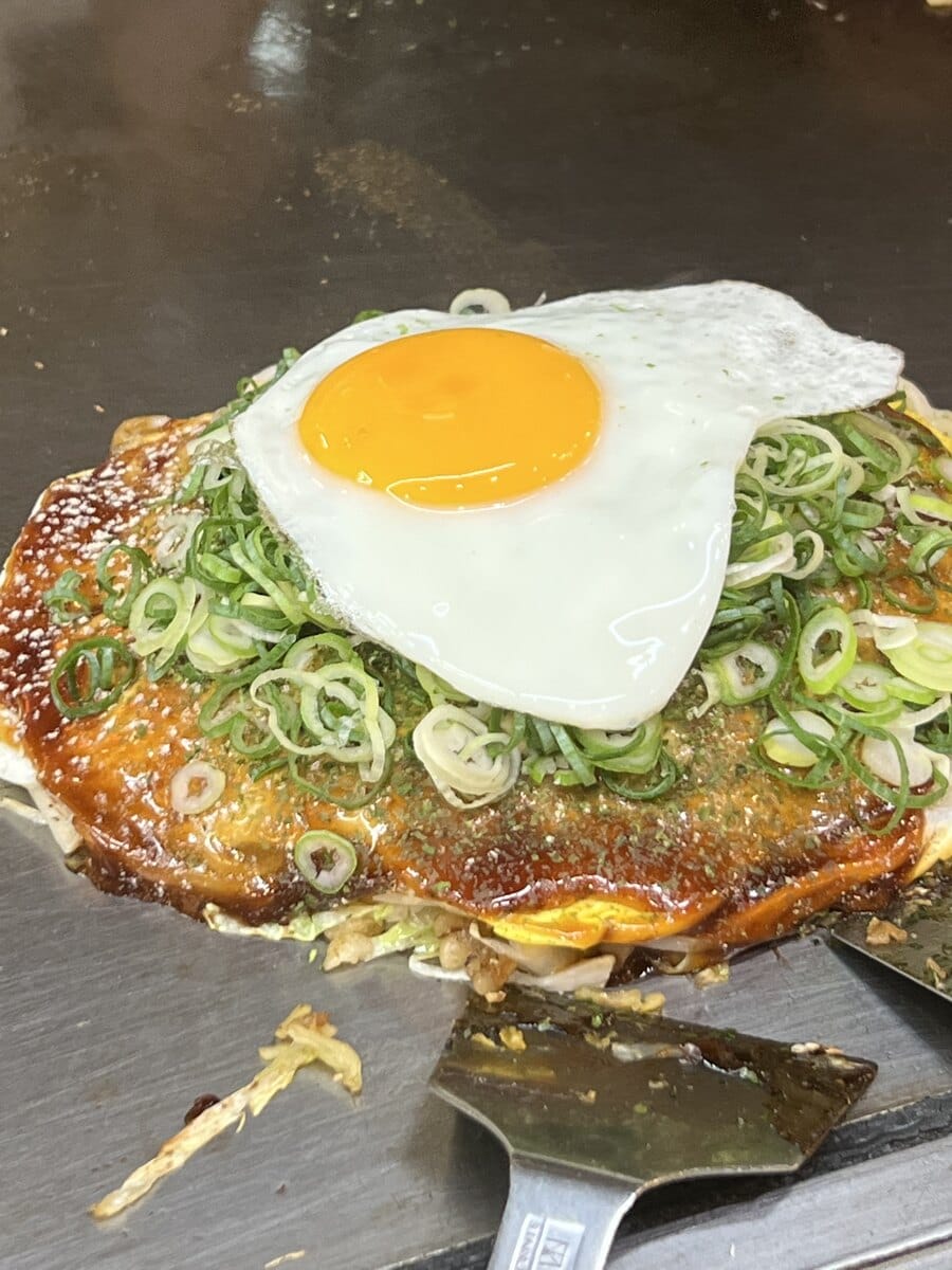 Hiroshima-style okonomiyaki on a hot plate with egg and green onion