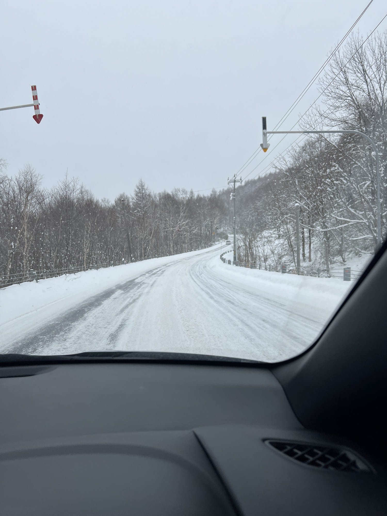 Route enneigée en direction de Kiroro vue depuis un pare-brise, avec des balises rouges et blanches au-dessus de la chaussée