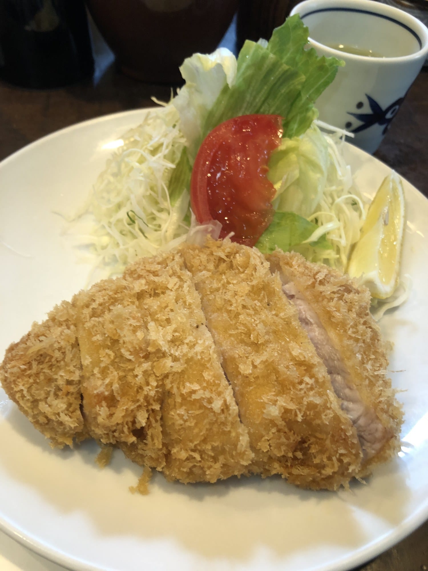 Thick-cut tonkatsu with shredded cabbage, tomato and lemon on a white plate at Marugo in Akihabara