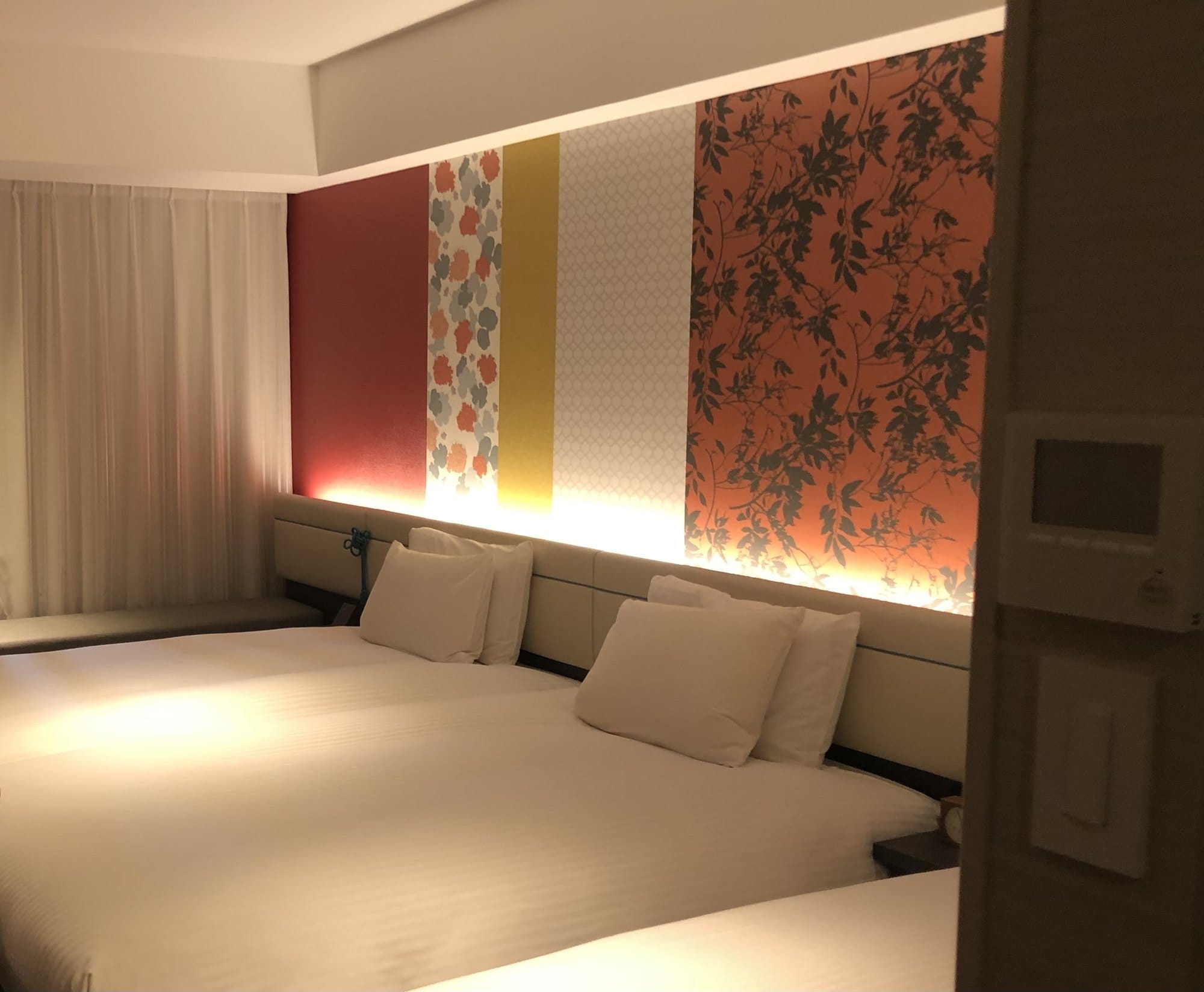 A twin room at Mitsui Garden Hotel Kyoto Shijo with a backlit floral and Gion Festival accent wall behind the beds