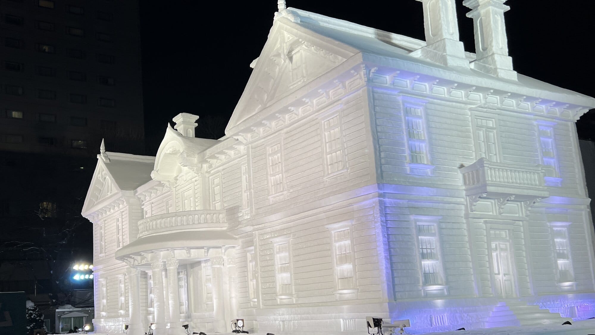 Large snow sculpture of a historic Western-style building illuminated at night in Odori Park during the Sapporo Snow Festival