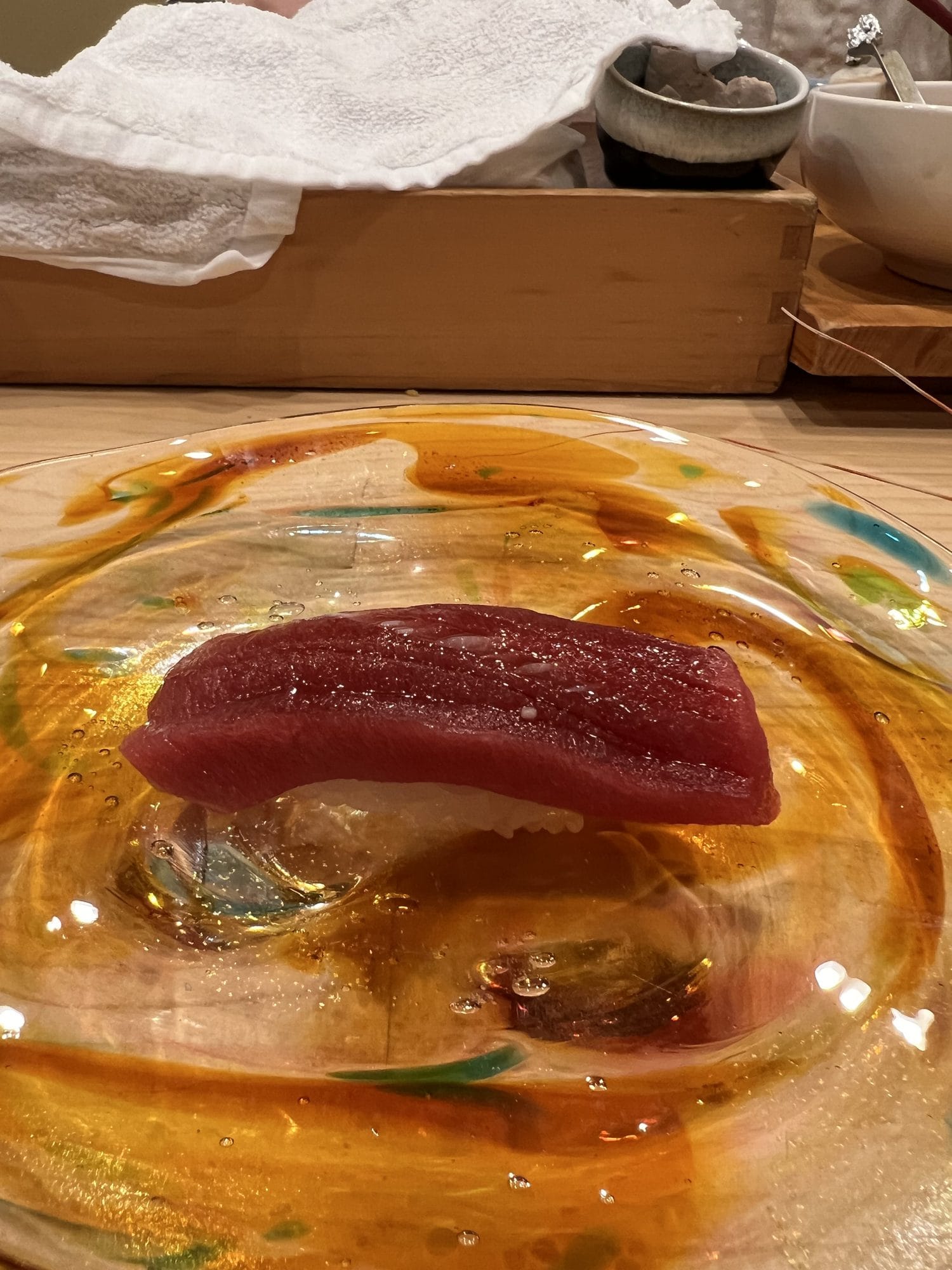 Single piece of tuna nigiri sushi served on a hand-blown glass plate at an Otaru sushi counter