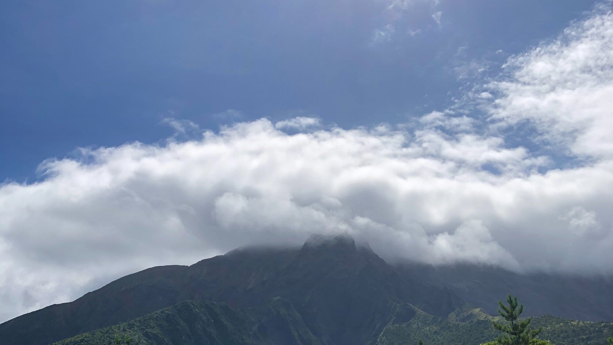 Sakurajima volcano partly covered by clouds beneath a bright blue sky