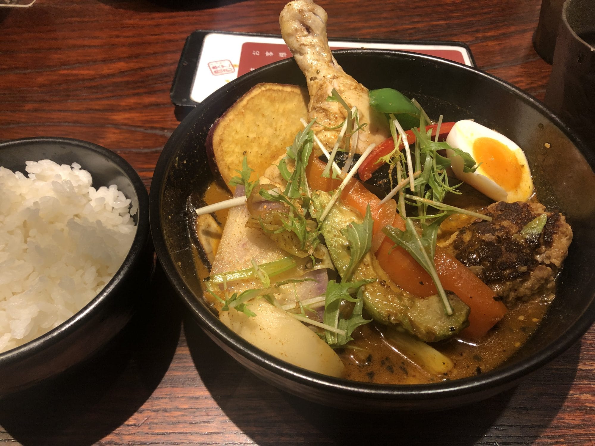 A bowl of Sapporo soup curry with chicken leg, vegetables, and a soft-boiled egg, served with steamed rice