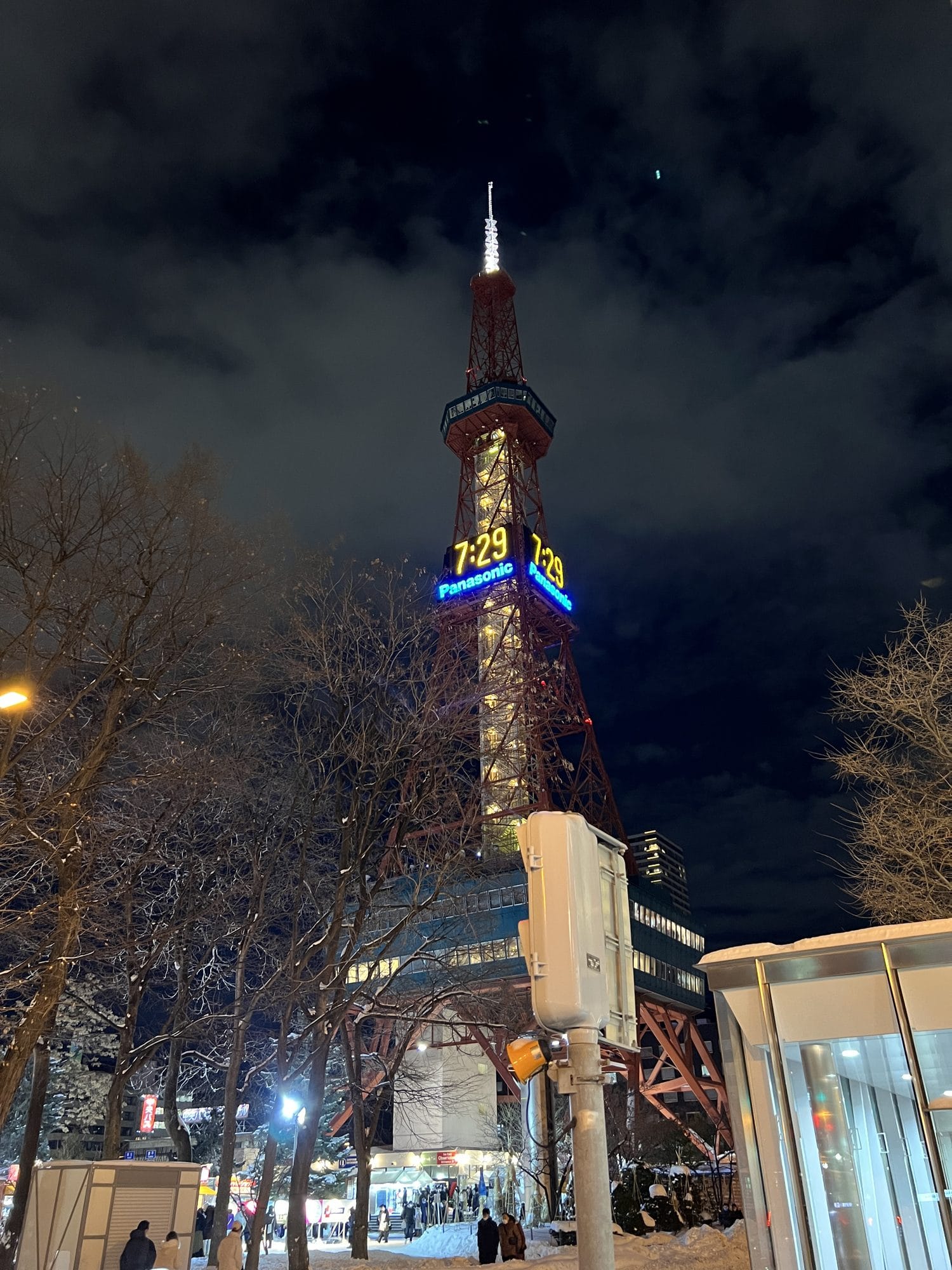 Sapporo TV Tower illuminated at night in winter, surrounded by snow-covered trees and streets