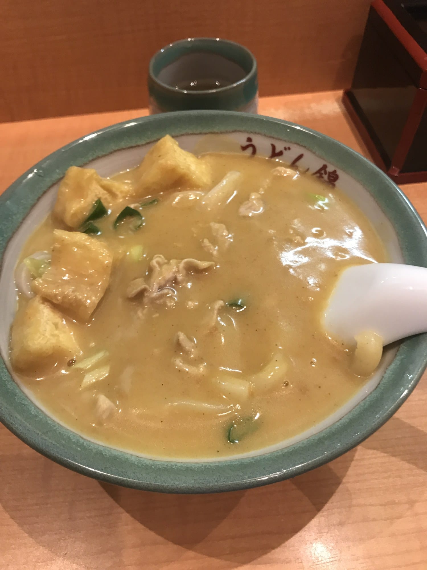 Creamy curry udon with fried tofu cubes and pork in a bowl marked Udon Nishiki