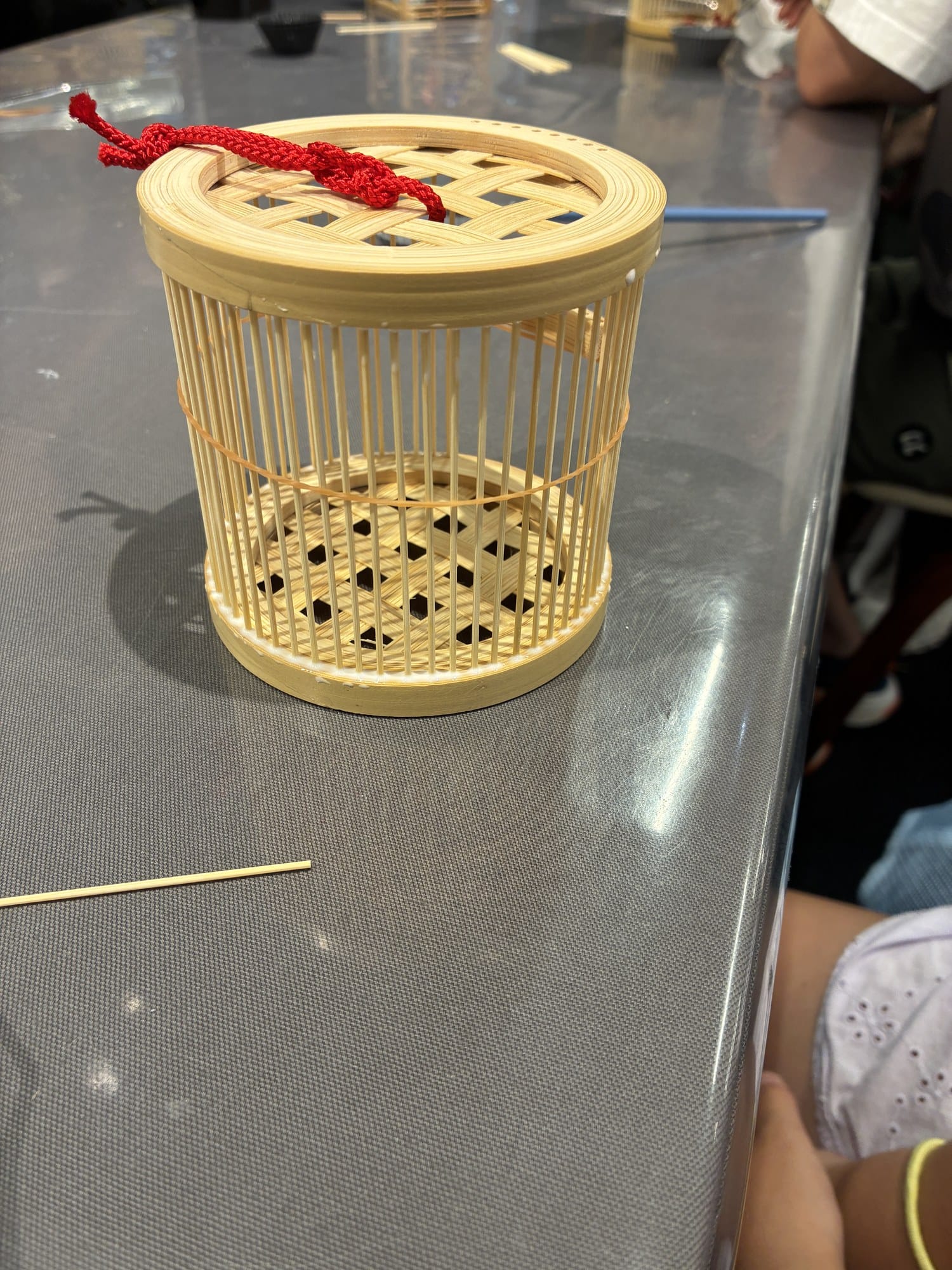 A completed bamboo insect cage with a red cord on a workshop table at Japan Traditional Crafts Aoyama Square in Tokyo