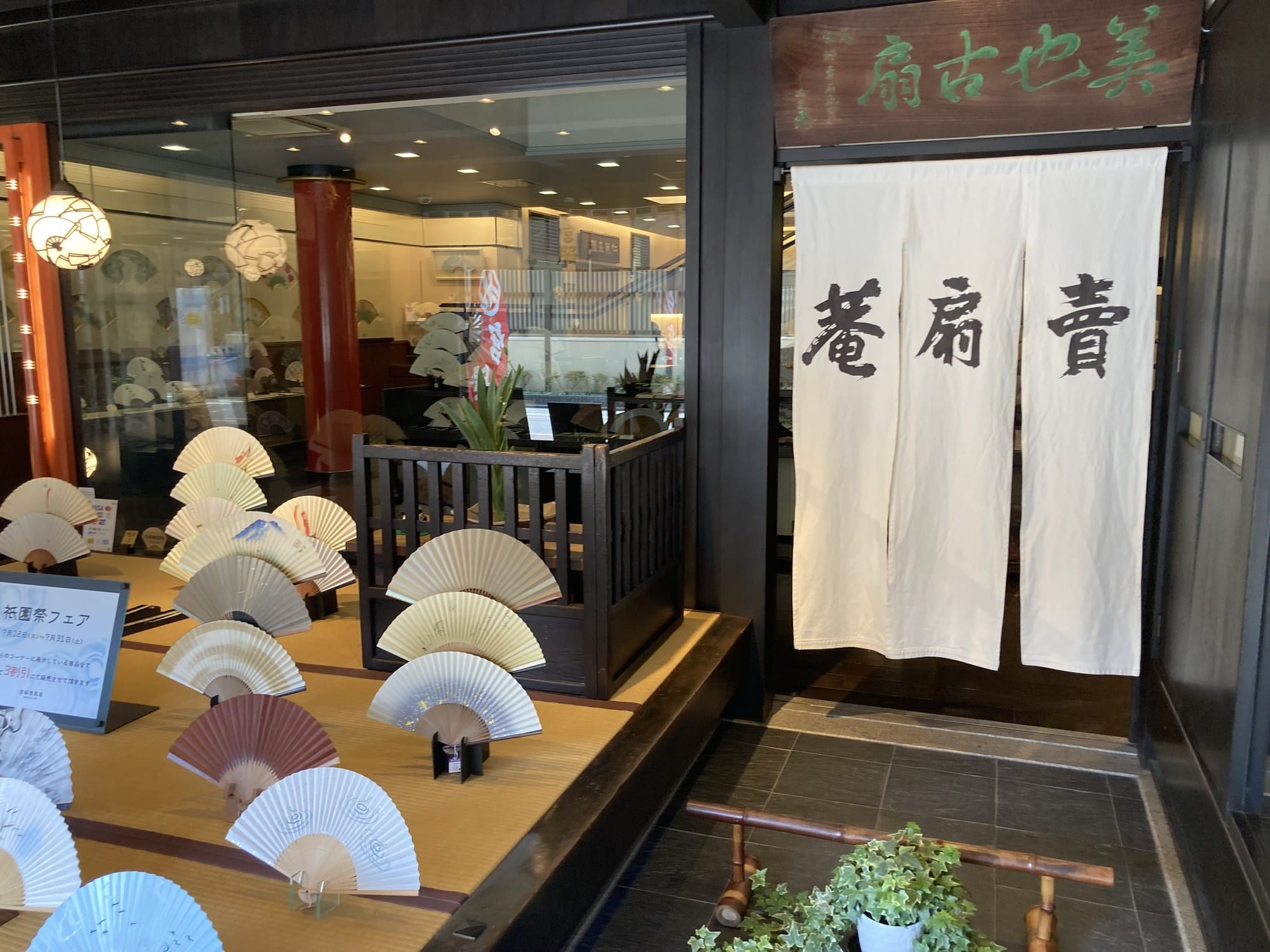 The street frontage of Miyawaki Baisen-an in Kyoto, with folding fans displayed open on tatami and a white noren curtain at the entrance