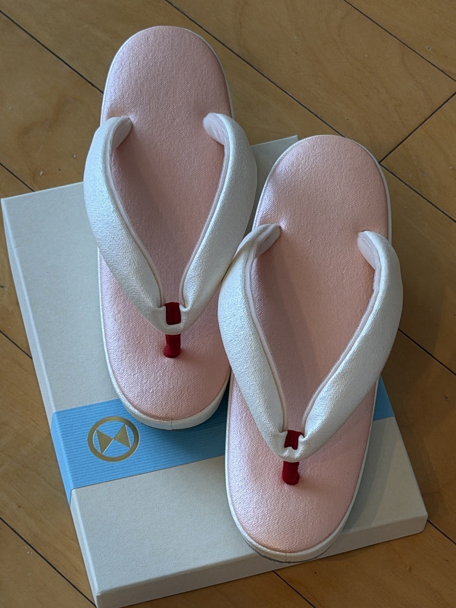 Made-to-measure zori seen from above, pink top with a white thong and a red toe post, on the Gion Naito box