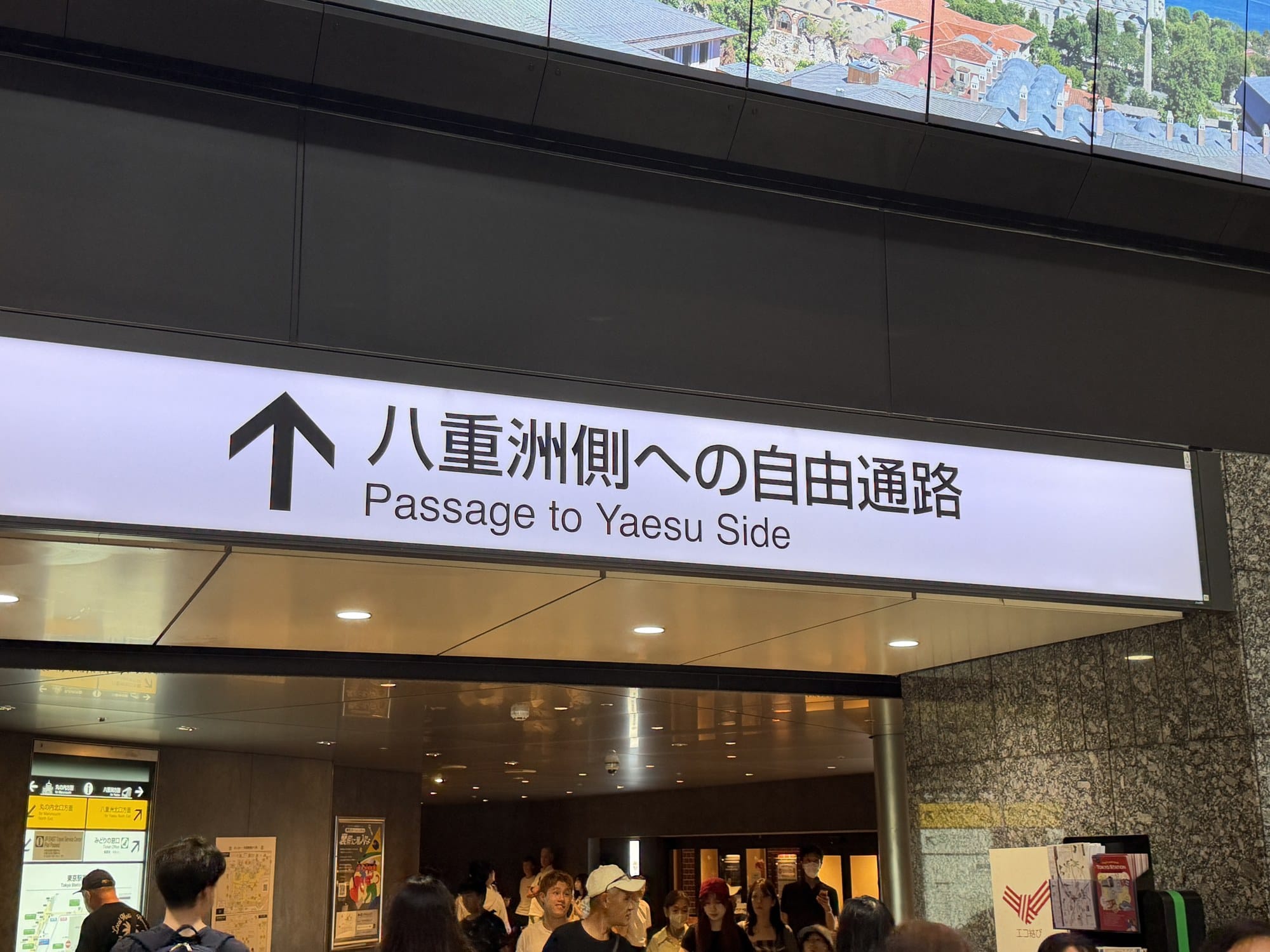Close-up of station signage inside Tokyo Station pointing to Marunouchi, Yaesu North Exit, the JR EAST Travel Service Center, and the Midori-no-Madoguchi ticket office