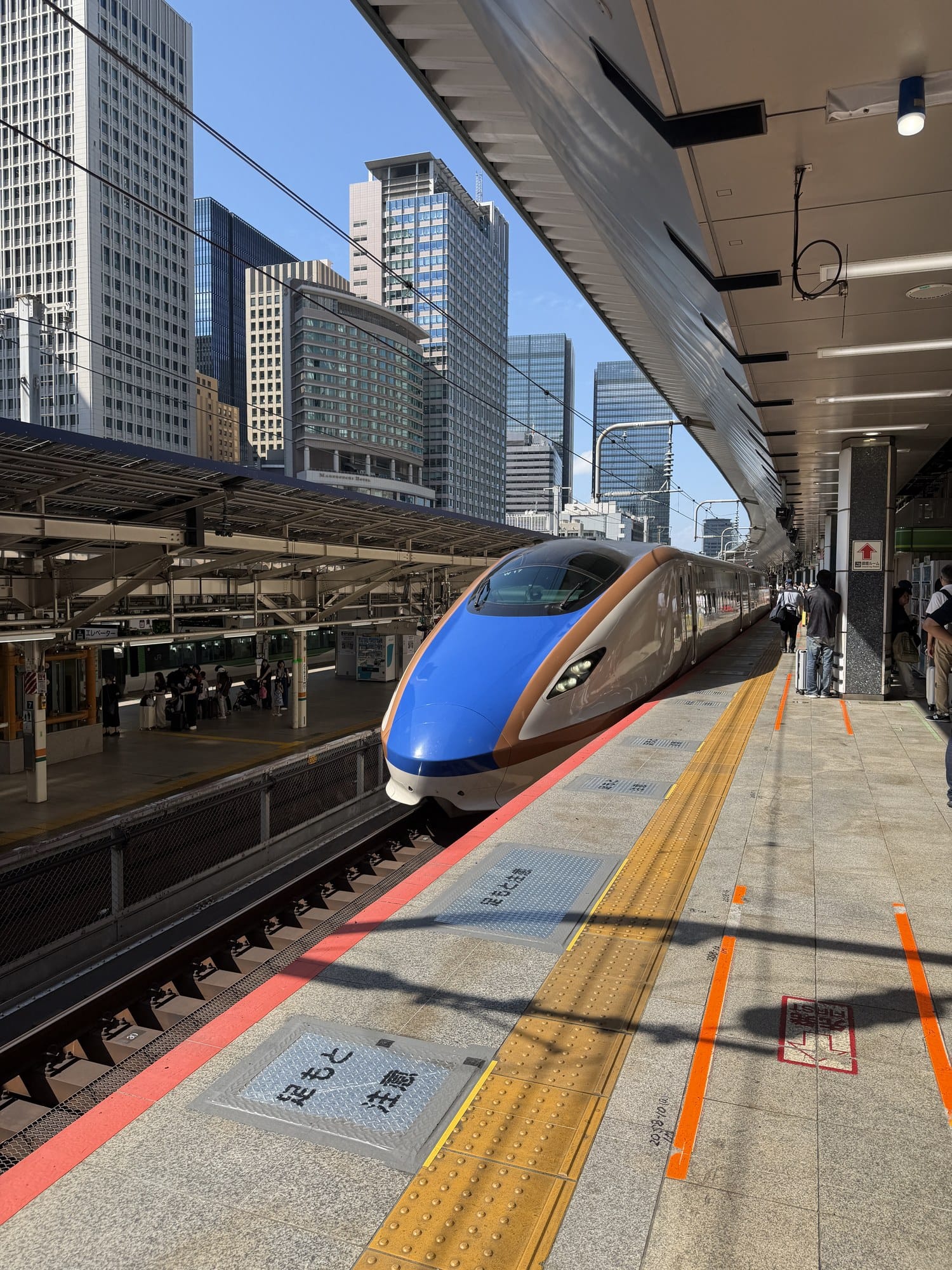 Blue and copper-accented E7/W7 series Hokuriku Shinkansen train at a platform