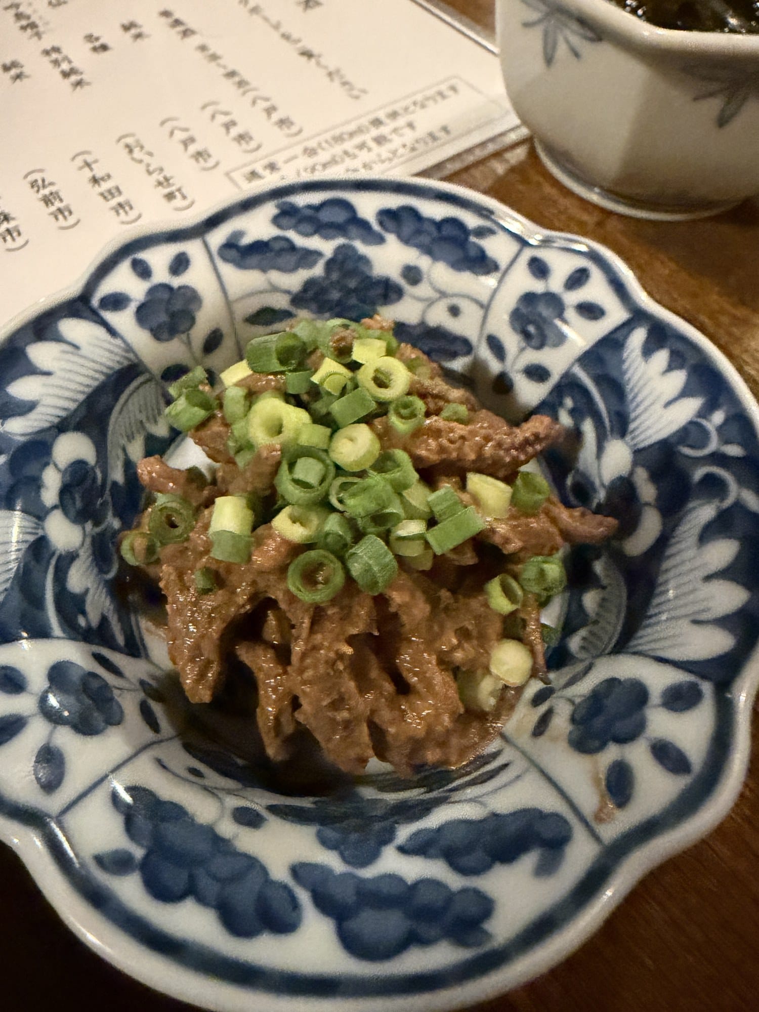 Ika no tomoae, squid in a liver-based sauce topped with chopped spring onion, in a blue-and-white dish at an izakaya in Hachinohe, Aomori