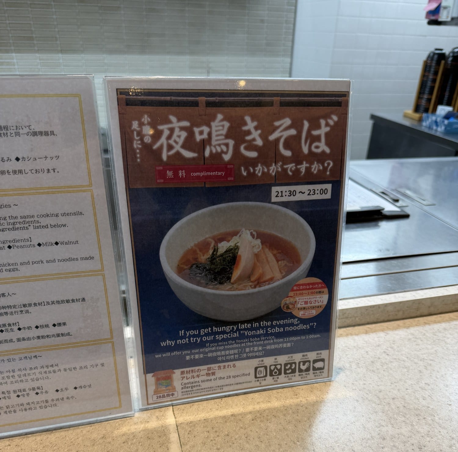 Hotel sign advertising complimentary yonaki soba noodles from 21:30 to 23:00, with English, Chinese and Korean text and allergen icons