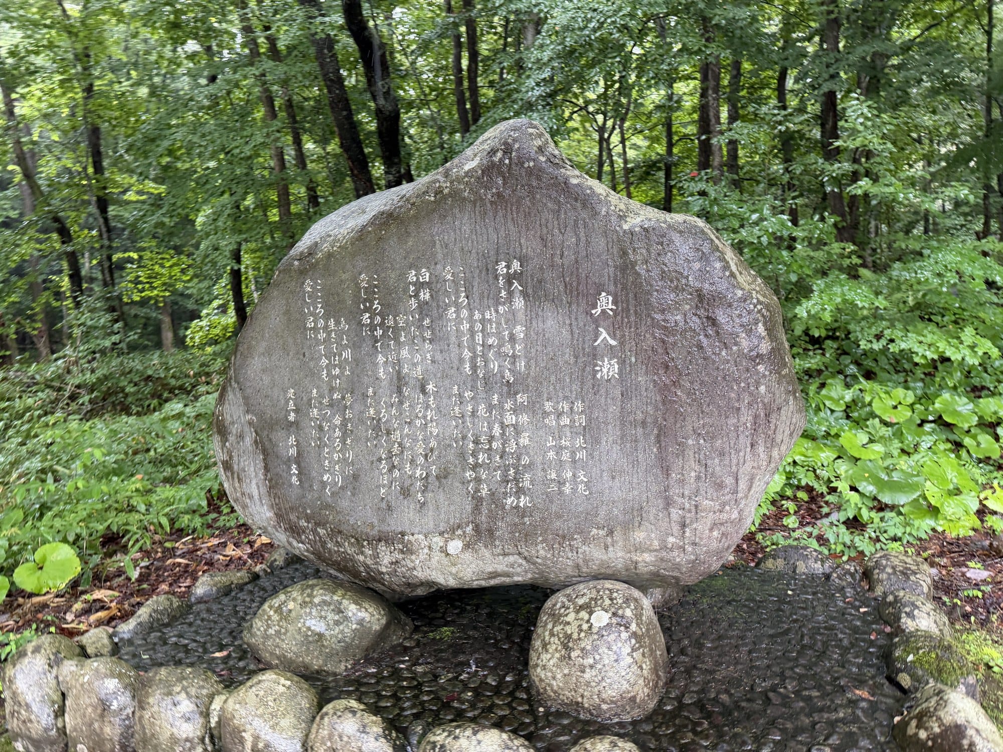 Mossy stone monument beside the walking path at Oirase Gorge in Aomori, with beech forest behind