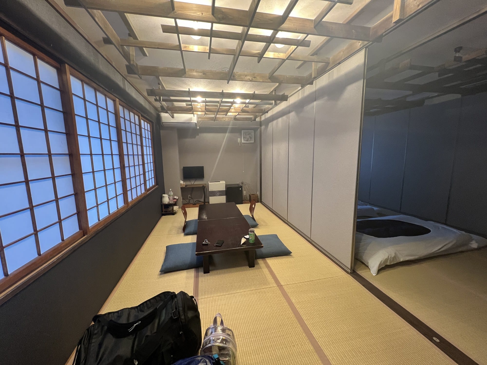 A long tatami room in a Japanese inn with a low table and floor cushions, and a futon laid out in the adjoining space behind sliding panels