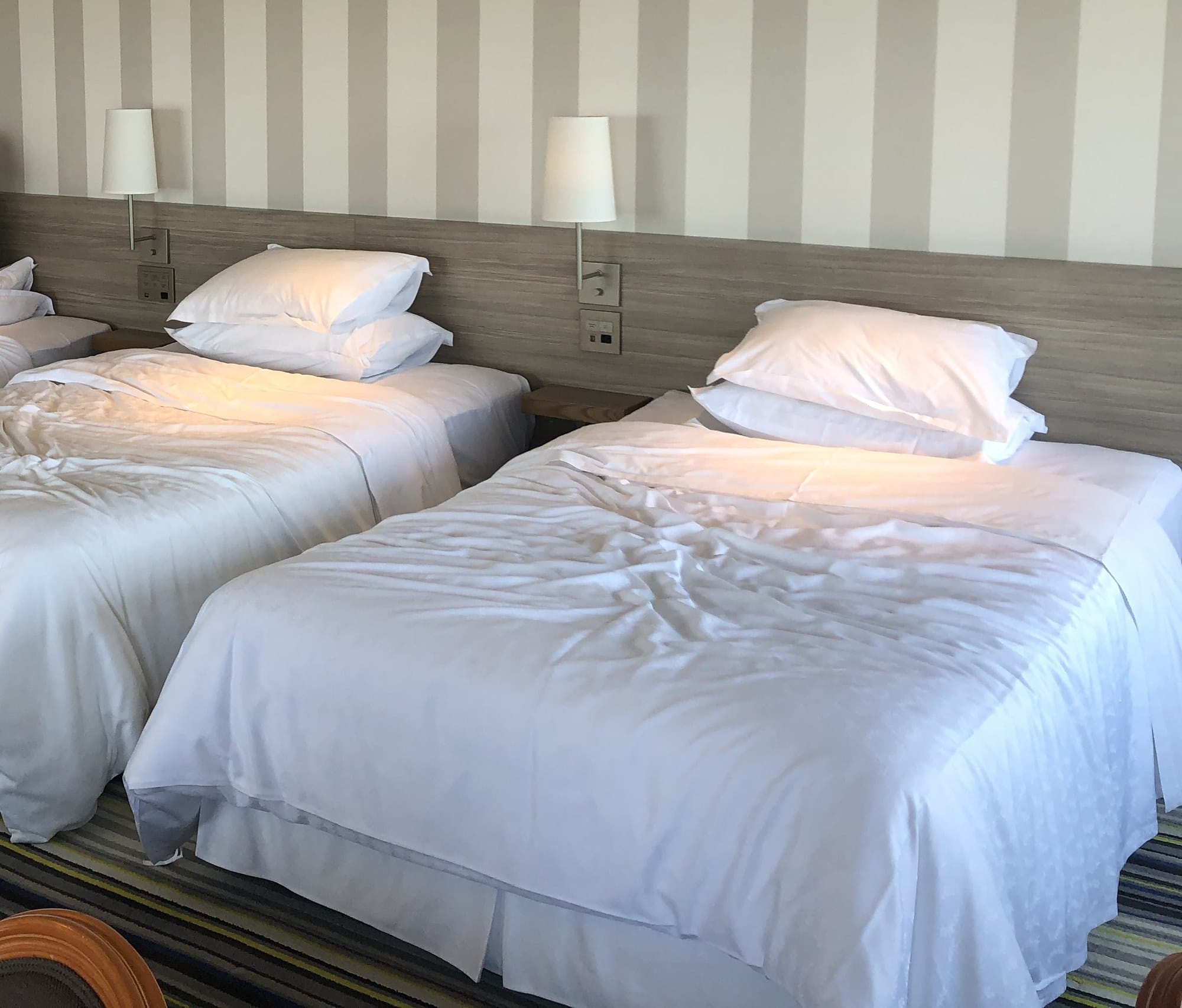 Three single beds lined up side by side against a striped wall in a bright hotel room