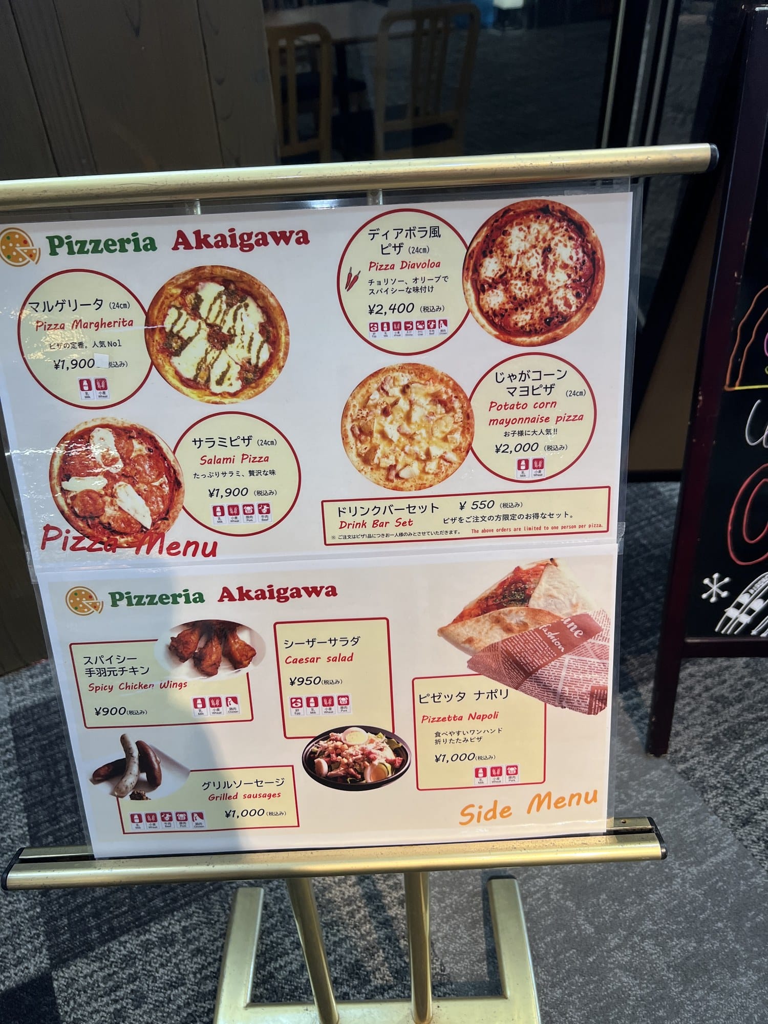 Menu board at Pizzeria Akaigawa at Kiroro listing pizza prices in Japanese and English