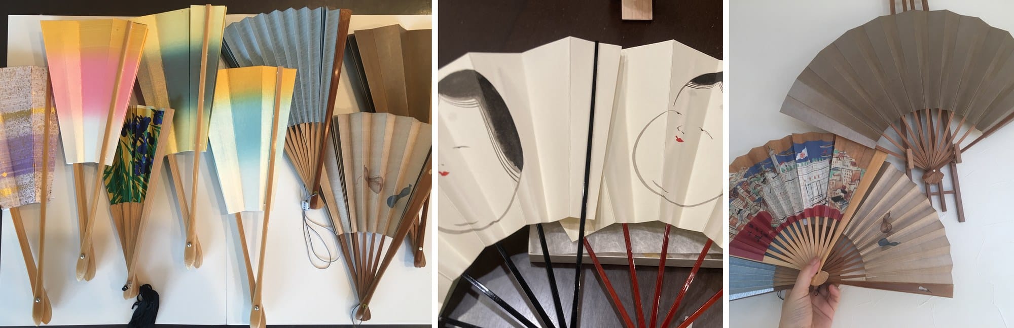 A row of Kyoto folding fans laid out flat, two fans painted with faces on black and red ribs, and a hand holding an open fan
