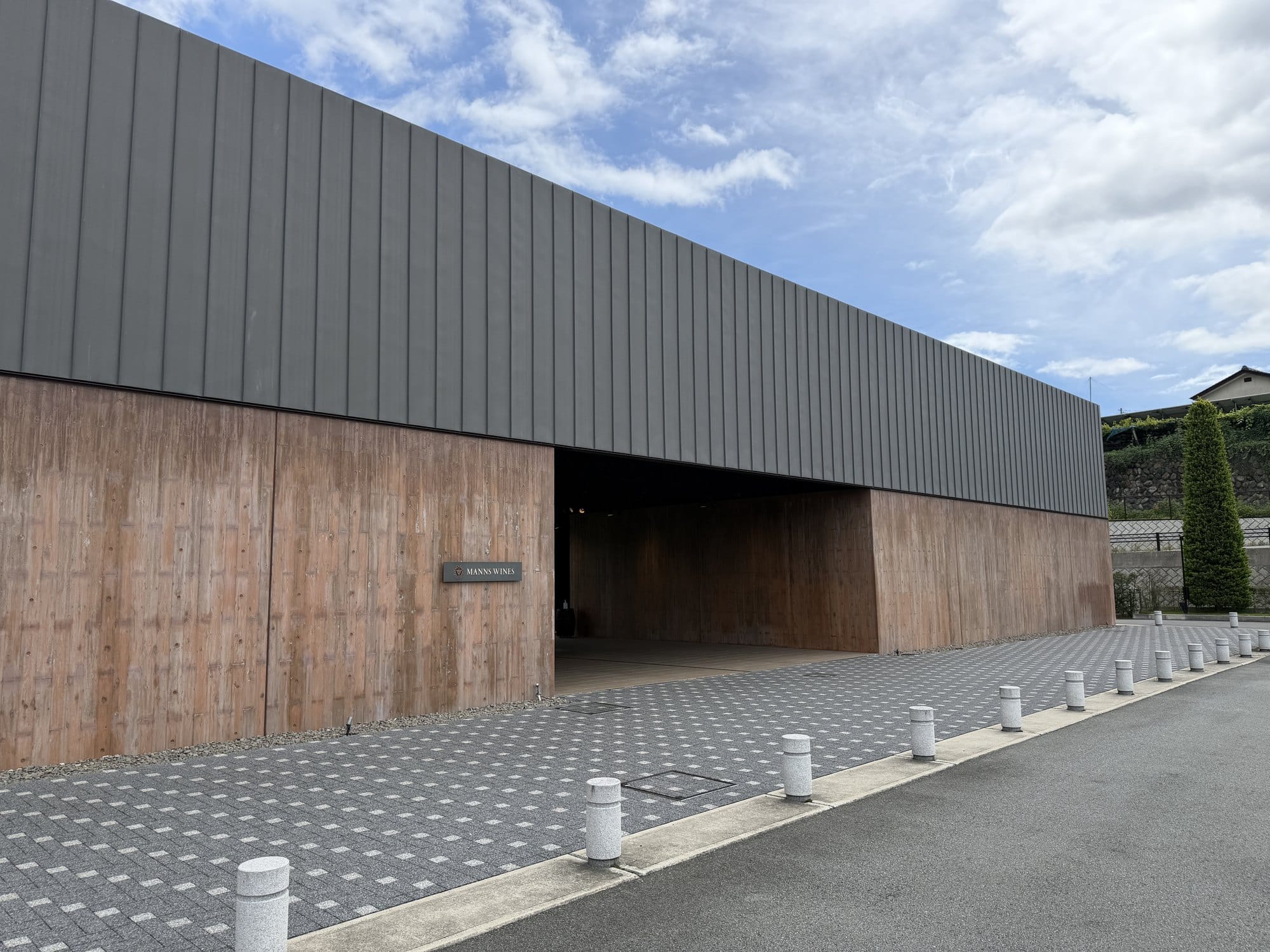The exterior of Mannns Wines Katsunuma winery in Yamanashi: a long low building with timber cladding below and dark metal above