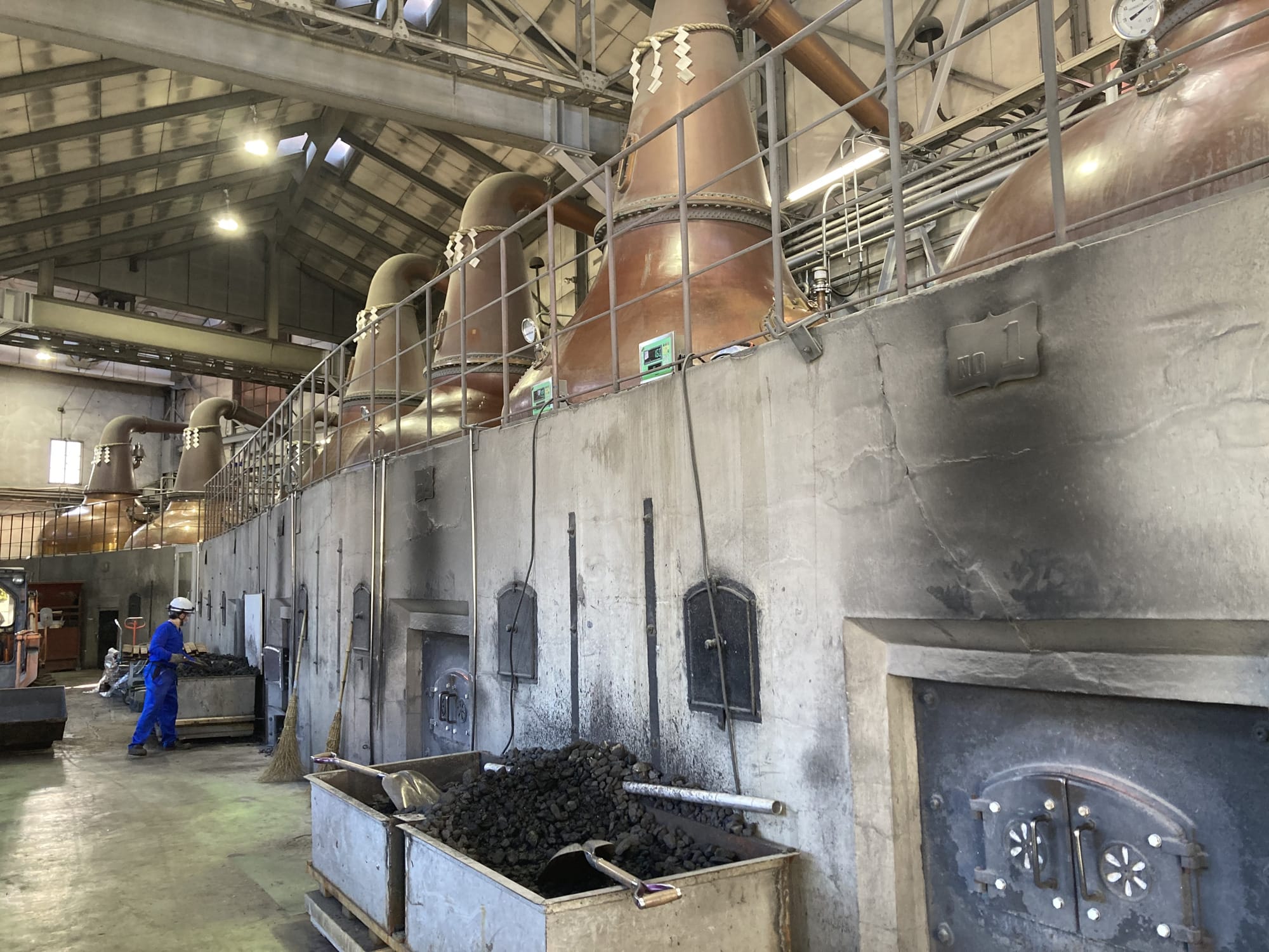 Copper pot stills with shimenawa ropes above the coal-fired kilns inside the Nikka Whisky Yoichi Distillery still house