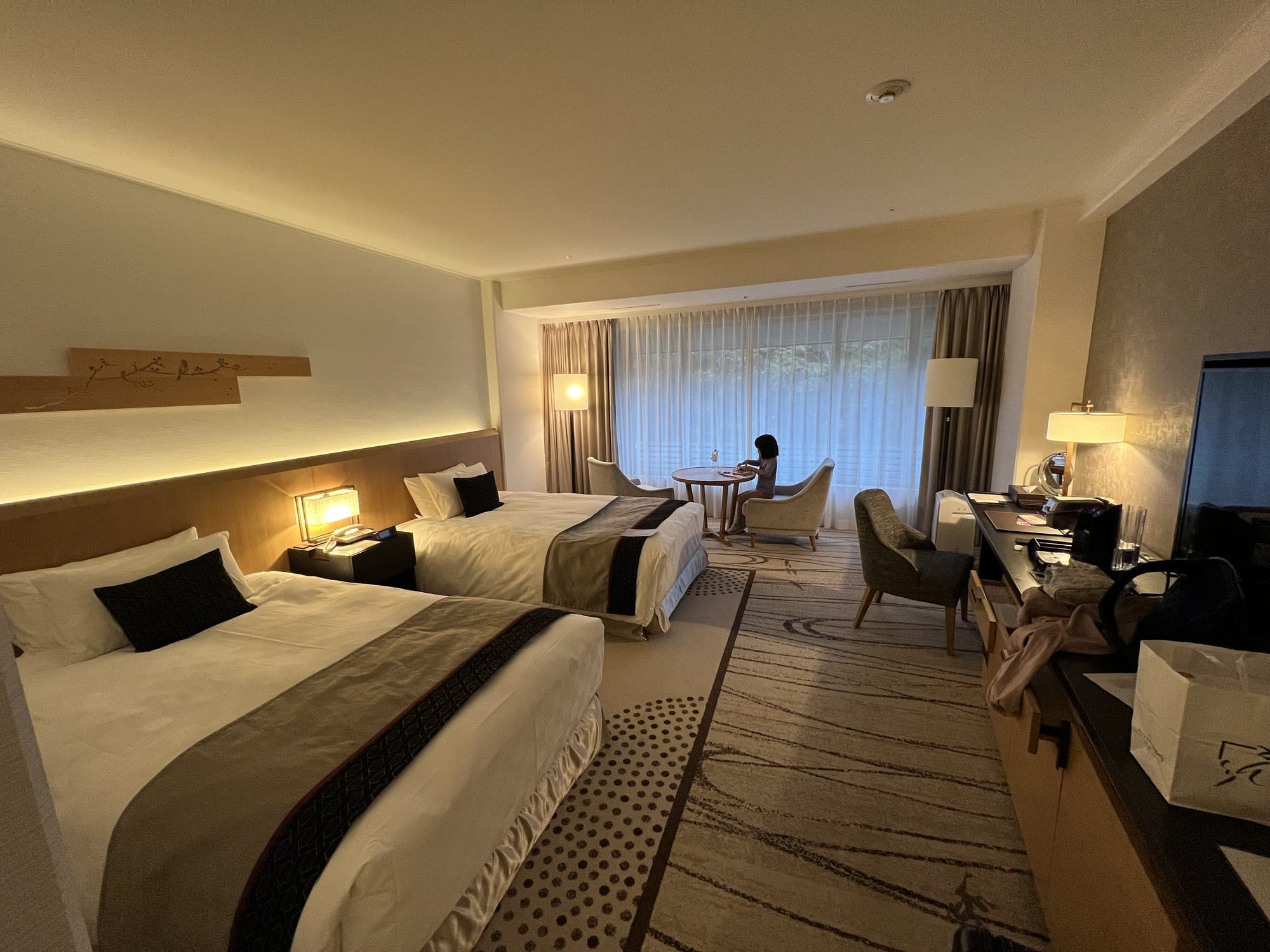 A twin room with two beds and a seating area beside a full-height window looking onto trees