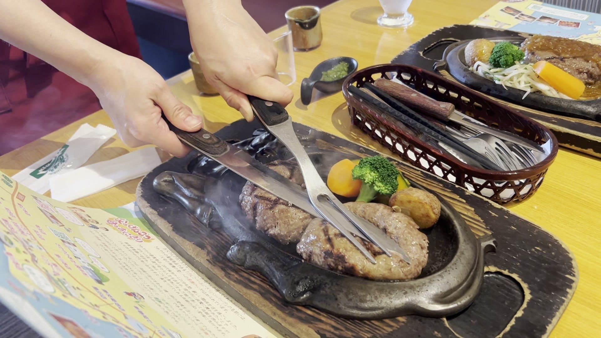 A server cutting a Sawayaka genkotsu hamburg in half at the table with a knife and fork