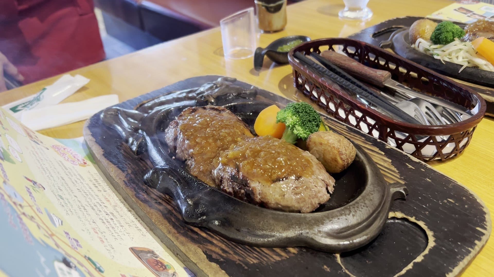 Onion sauce being poured over the seared faces of a Sawayaka hamburg on the hot plate, steam rising