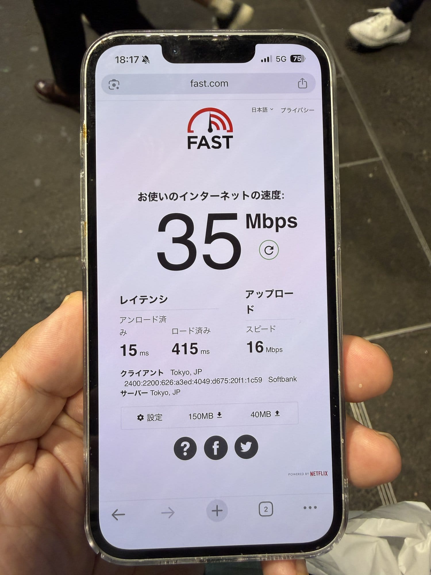 iPhone 16e held at street level near Shibuya Scramble Square showing a fast.com result of 35 Mbps on SoftBank 5G