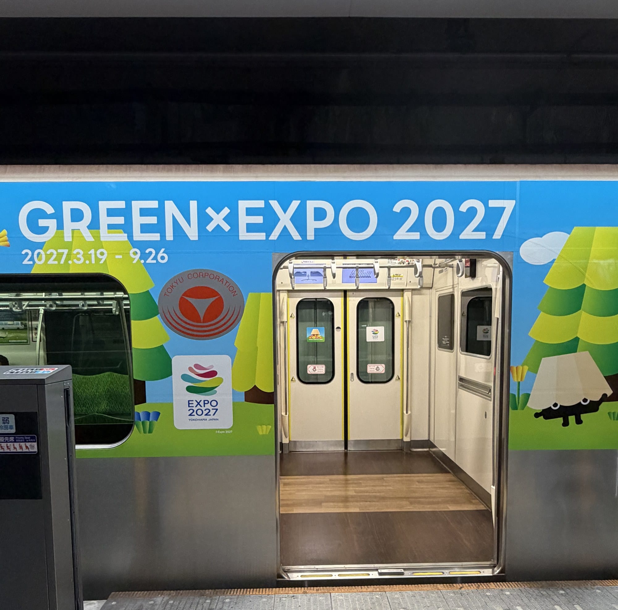 A Tokyu train wrapped in GREEN×EXPO 2027 livery with doors open at a platform, showing the Tokyu Corporation crest beside the official EXPO 2027 Yokohama Japan logo and the dates 2027.3.19 - 9.26