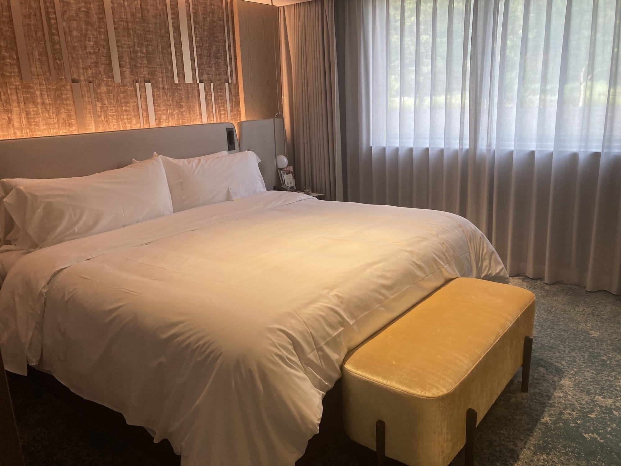 A king room at The Westin Miyako Kyoto with a patterned timber headboard wall, white bedding and a mustard bench at the foot of the bed