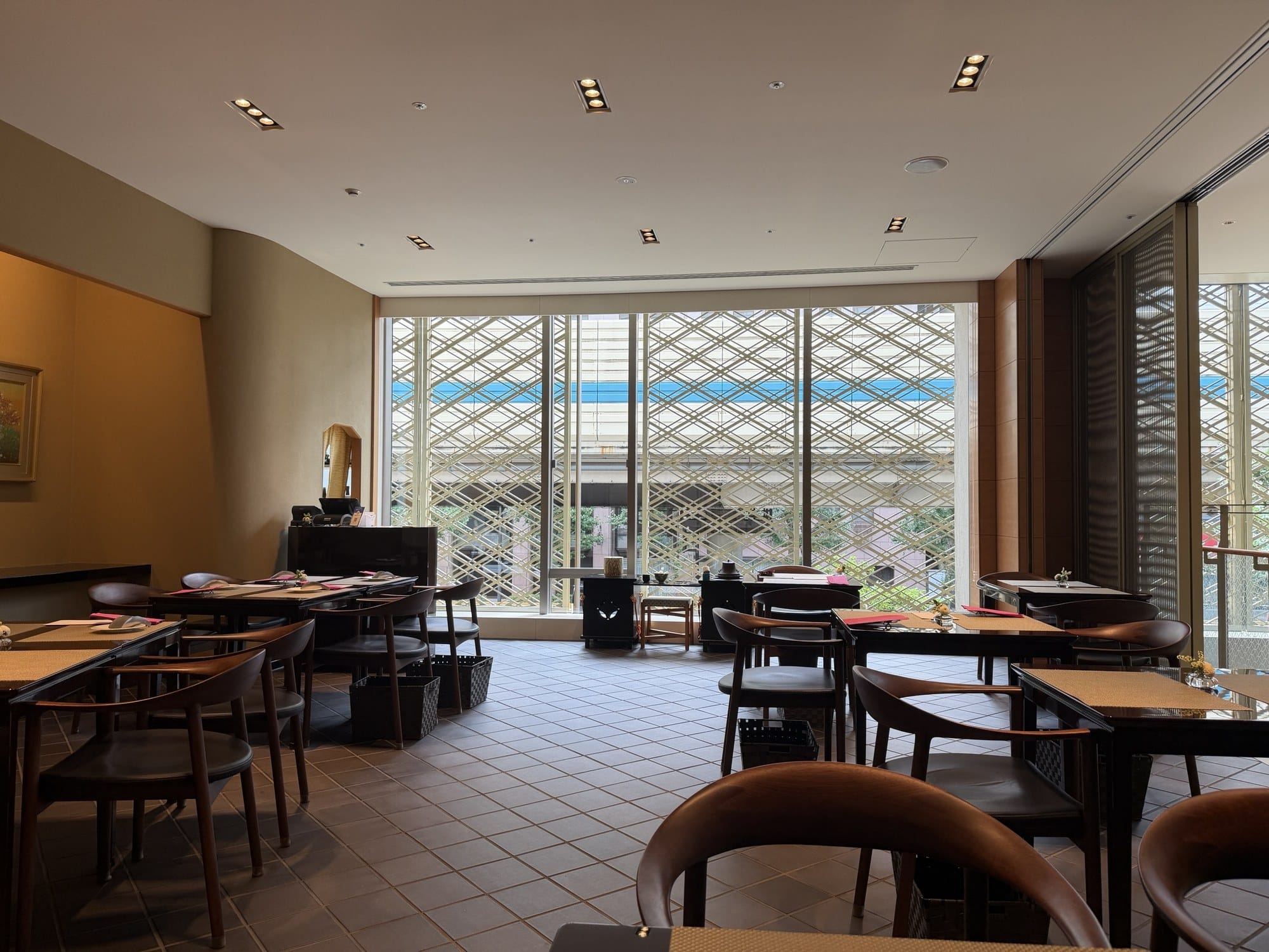 Tea Lounge Kafu's dining room with bentwood armchairs, a table set with a placemat, and a floor-to-ceiling lattice window behind, no guests in view
